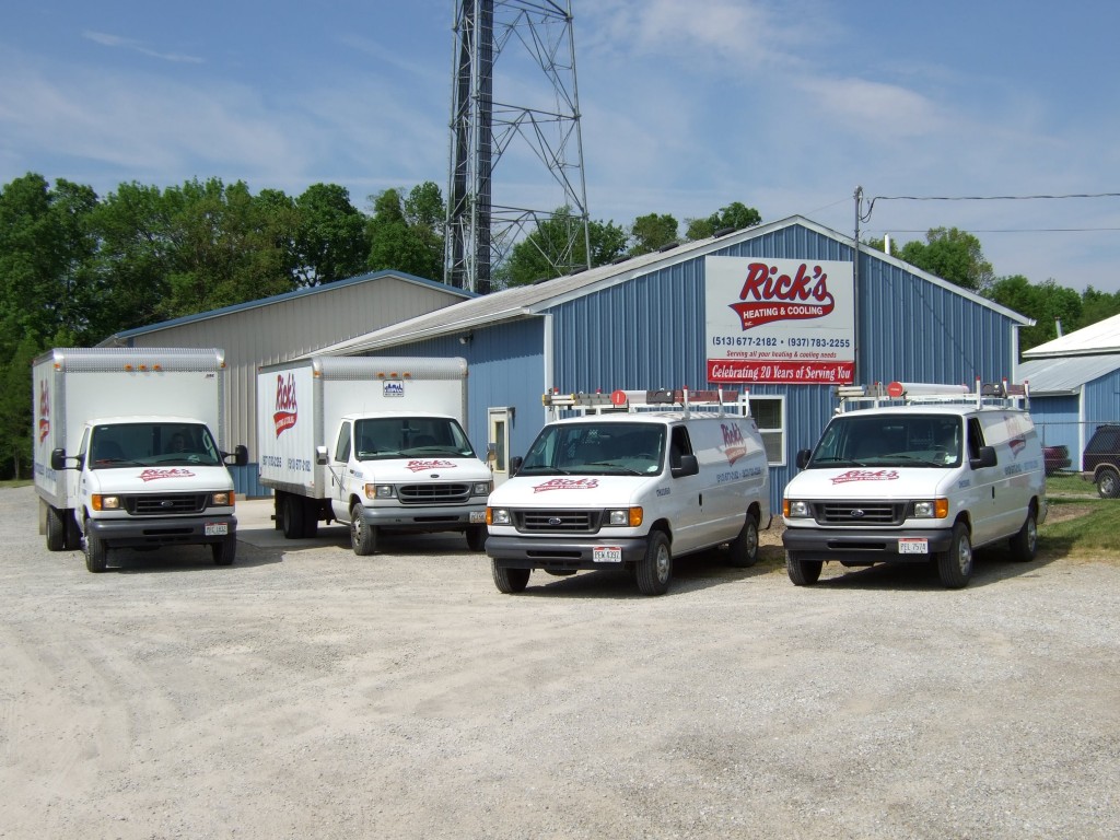 Rick's Heating & Cooling service trucks parked in front of a blue metal building with a Rick's Heating & Cooling sign.
