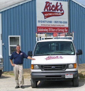 Employee standing next to Rick's Heating & Cooling service van, in front of building.