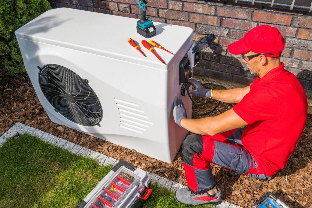 HVAC technician repairing a heat pump outside a home
