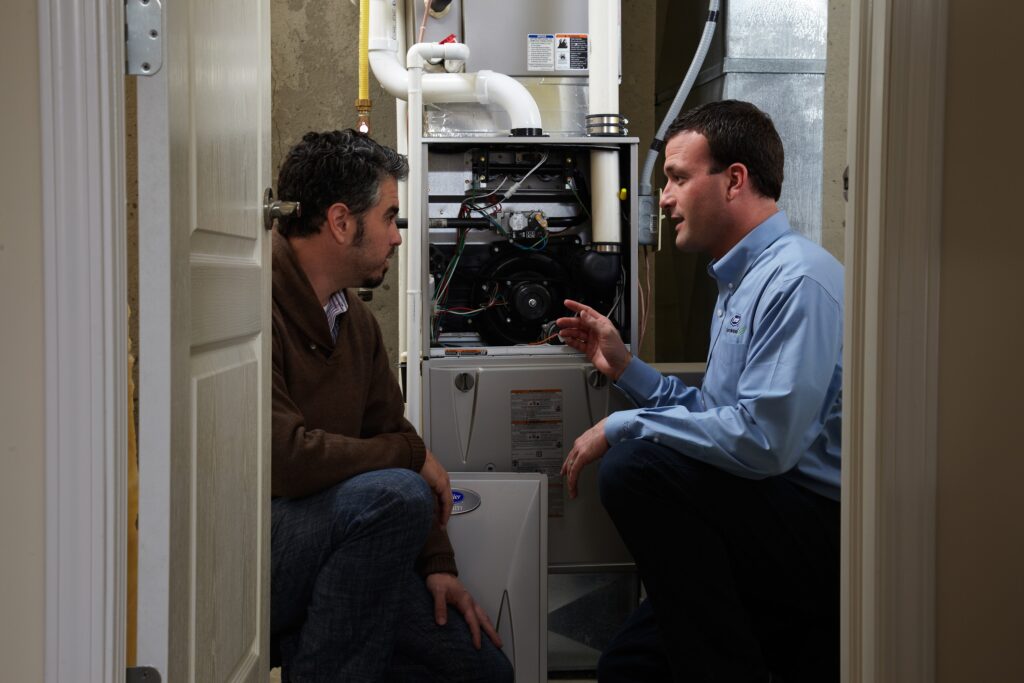 HVAC technician and homeowner talking in front of a furnace